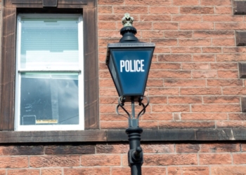 A police lamp post in front of a brick building, with a window to the left, indicating a police station or office.